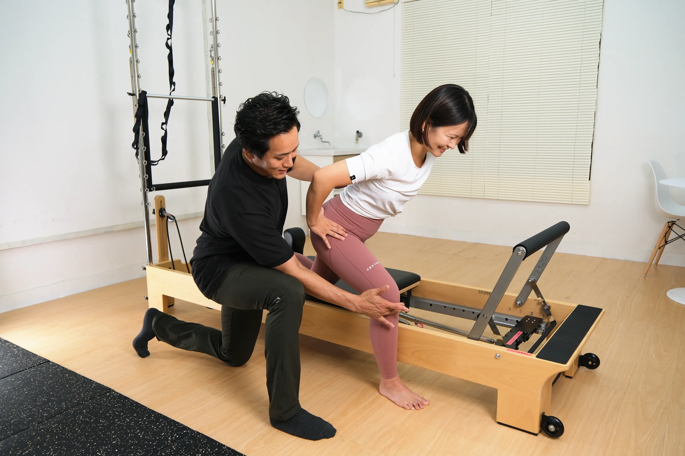 タワー付きのリフォーマーで、トレーナーが脚の動きを確認しながら指導している様子