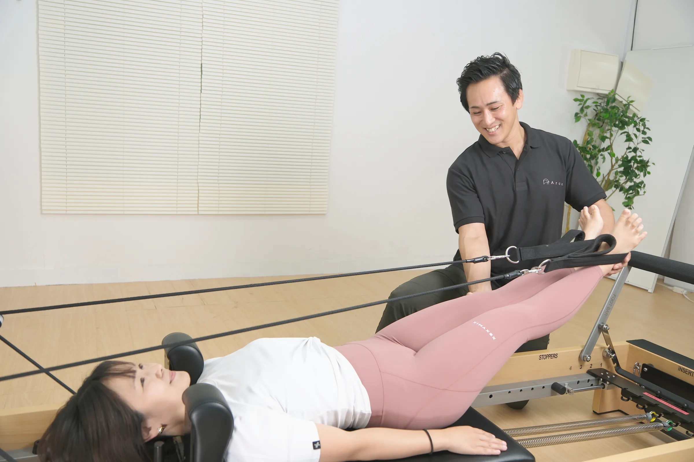 トレーナーの声かけを受けながら、リフォーマーでストラップを使った動きを体験する女性