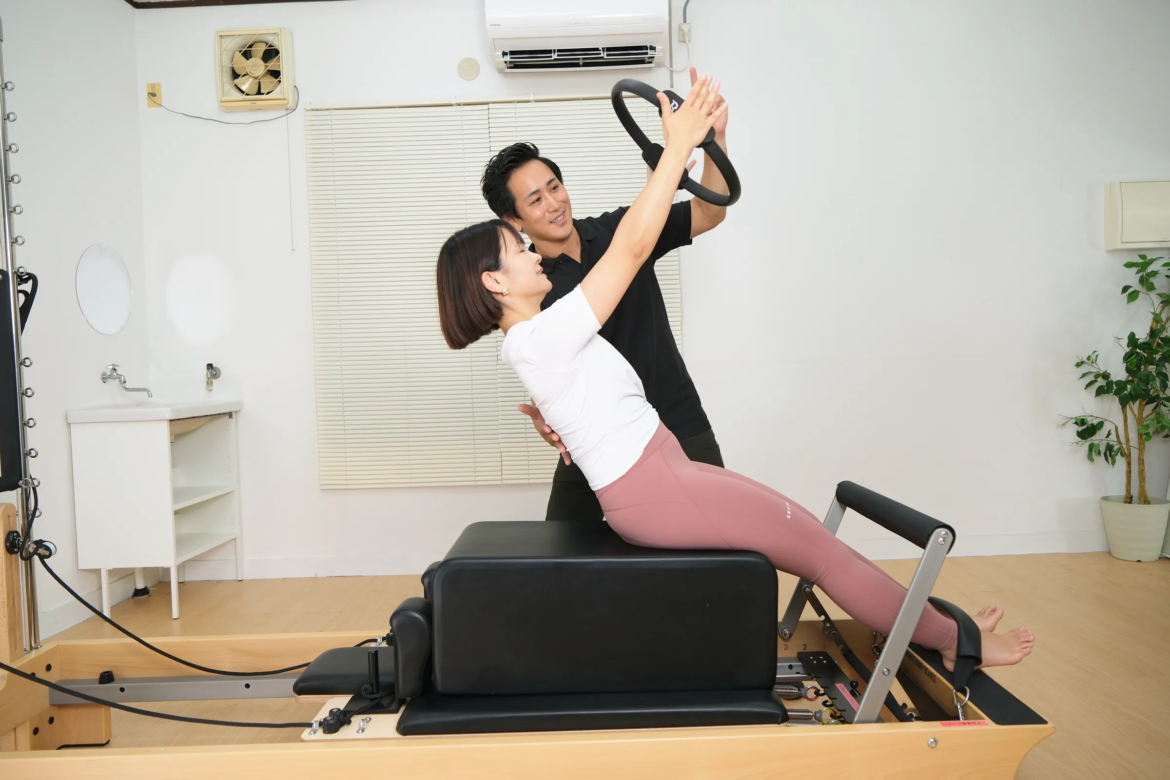 ピラティスリングを使い、トレーナーの補助で上体を伸ばすマシンピラティスの様子