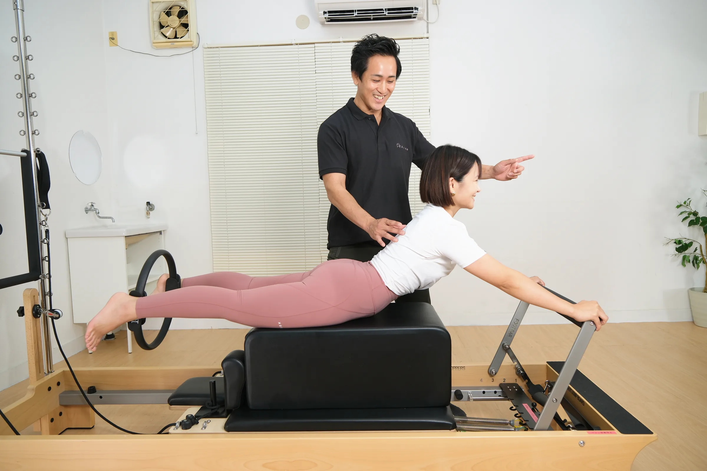 ボックスの上でうつ伏せになり、トレーナーの声かけで背中を伸ばしているマシンピラティスの動作