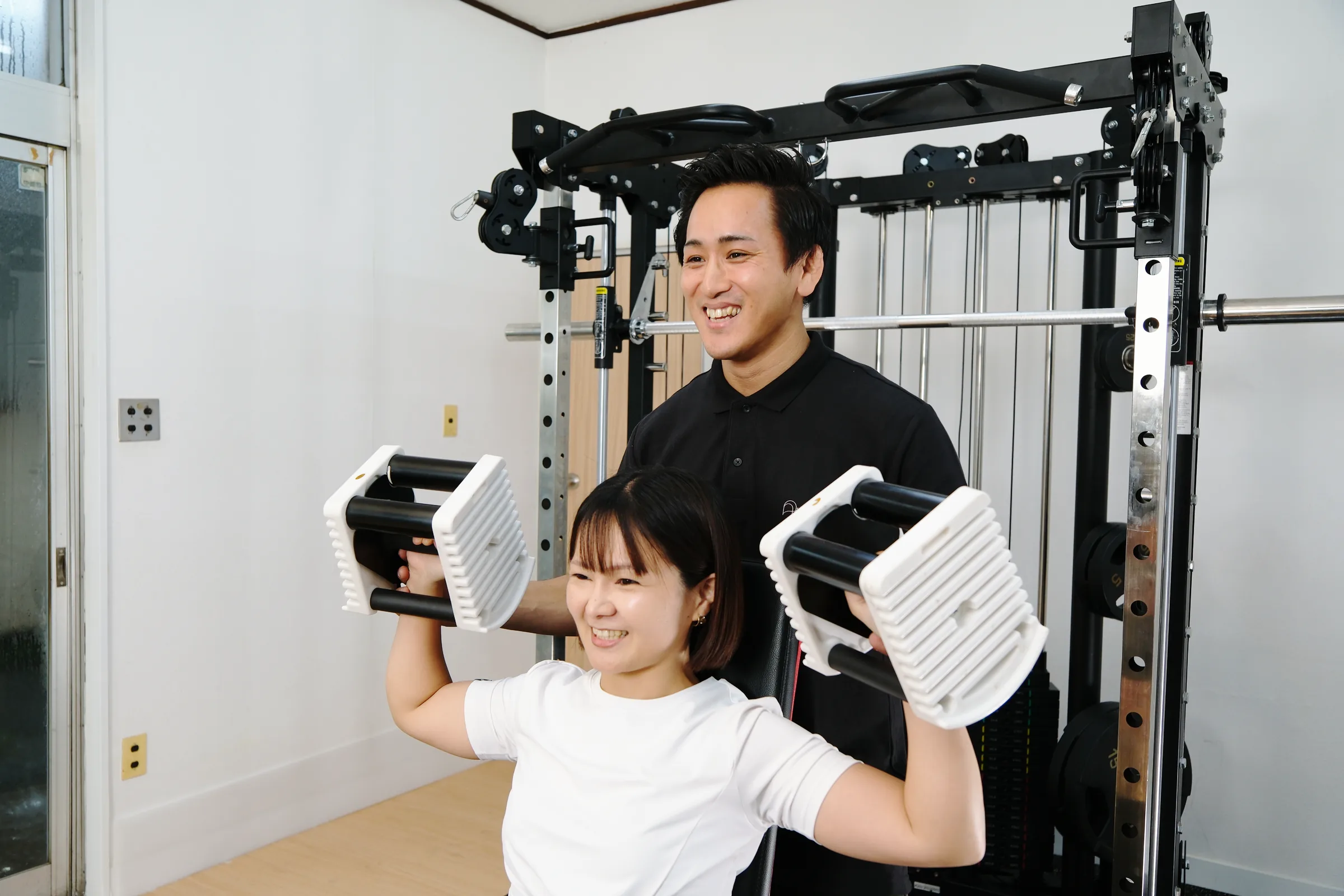 トレーナーのサポートを受けながら、ダンベルでトレーニングに取り組む女性